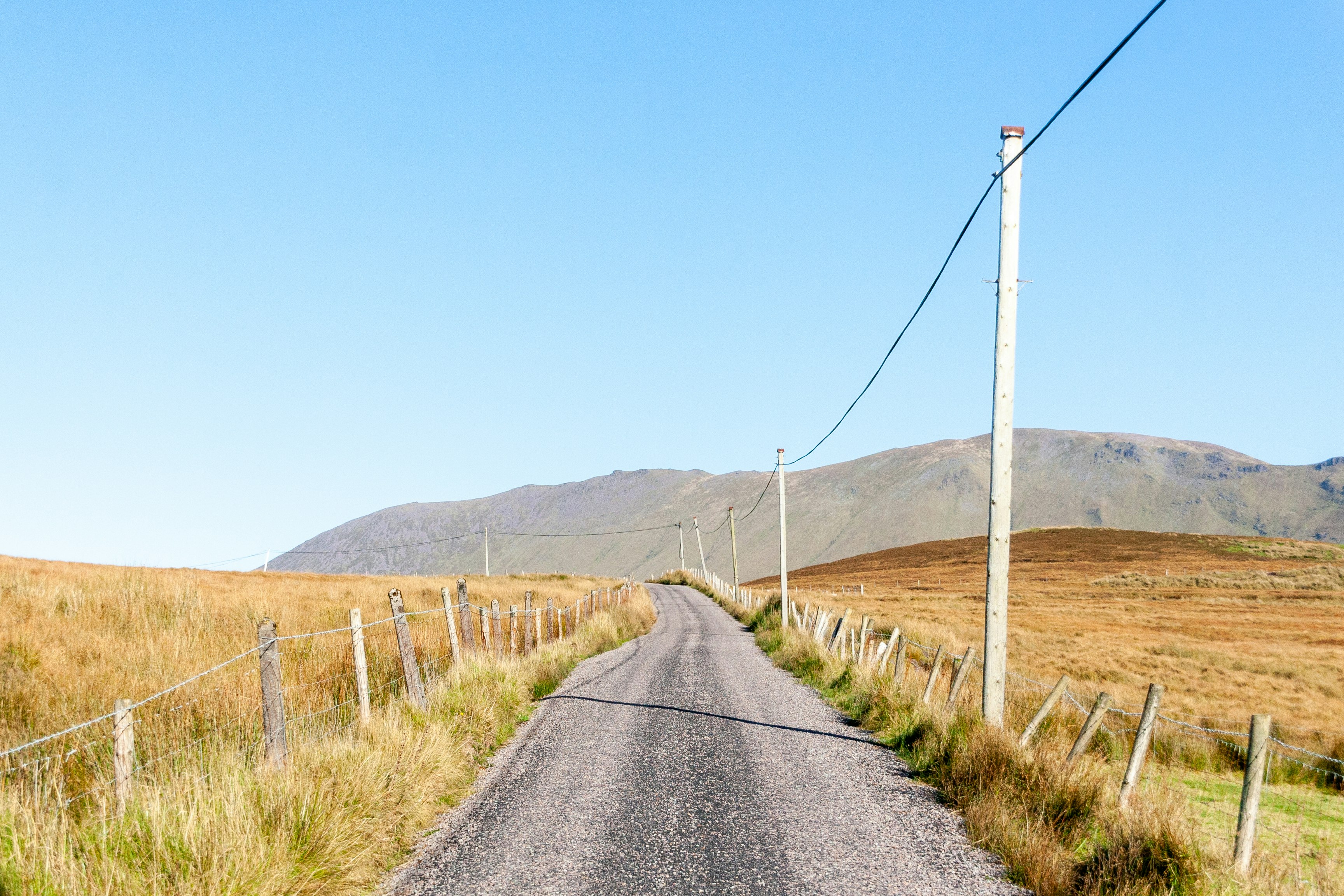 gray asphalt road between brown grass field during daytime